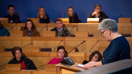 People sitting in a conference centre with a woman talking into a microphone