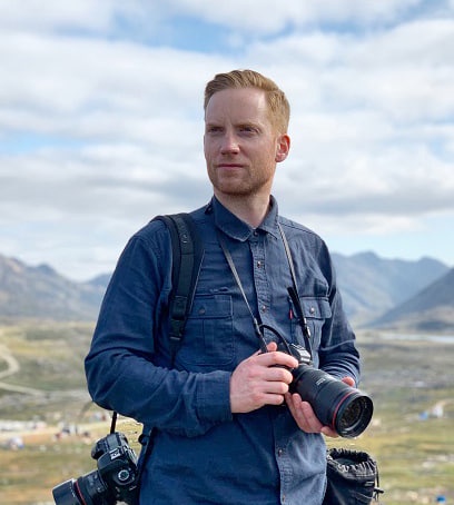 Red-haired man holding two cameras in the countryside